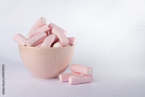 Pink Bowl Overflowing with Marshmallows and a Pile of Sweets to the Left on a Crisp White Horizontal Background