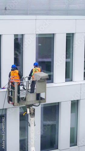 Two workers wearing safety harness wash office building facade at