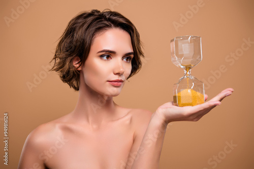 Photography Photo of charming attractive lady nude shoulders holding hourglass isolated beig