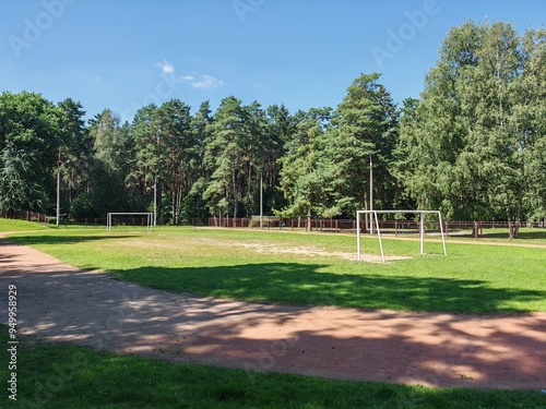 Wallpaper Mural A children's dirt soccer field with metal gates and a dirt running track is located near the city park and is surrounded by a metal fence. It is surrounded by pine and birch trees Sunny summer weather Torontodigital.ca