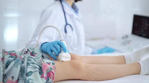 Doctor and kid patient. Orthopedist wearing blue protective gloves performing ultrasound examination on a child's knee in a clinic. Medicine photo