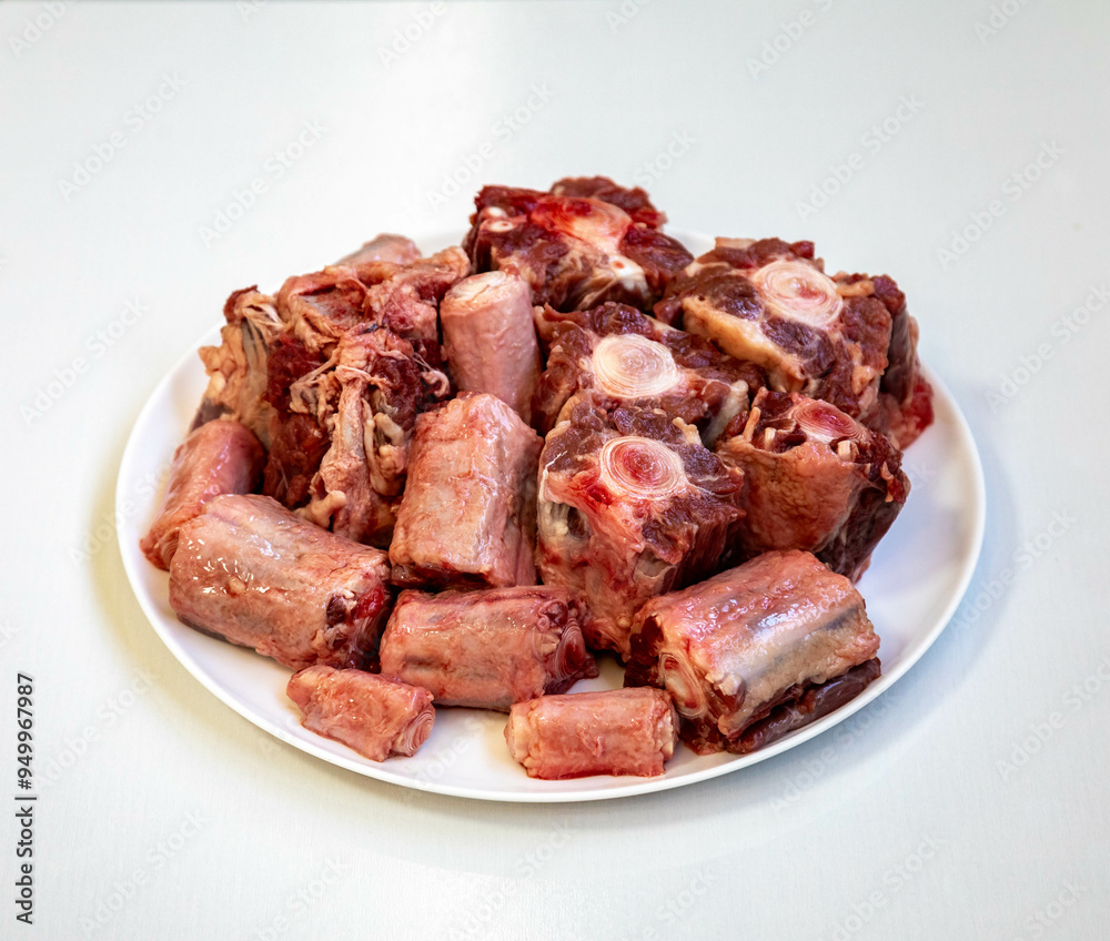 Raw beef oxtail on a round white plate in closeup. Raw beef oxtail on a round white plate in closeup.