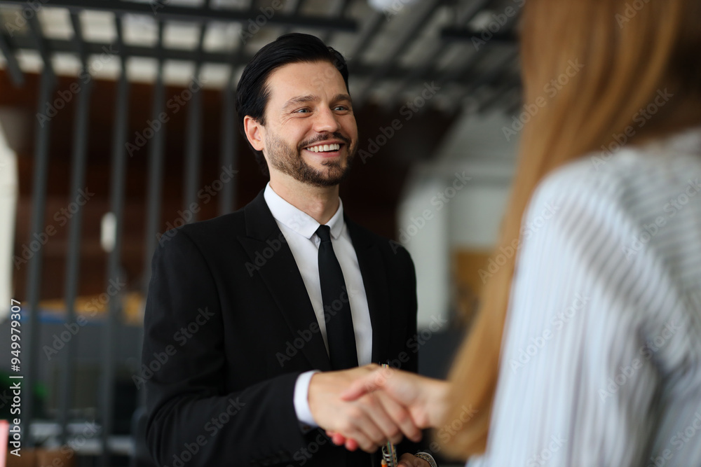 A man in a suit shakes hands with a woman. The man is smiling and the woman is smiling back. Scene is friendly and positive A man in a suit shakes hands with a woman. The man is smiling and the woman is smiling back. Scene is friendly and positive