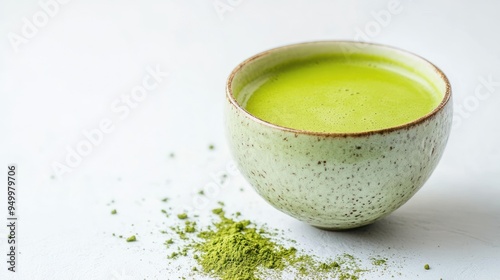 A ceramic bowl filled with vibrant green matcha tea, with matcha powder sprinkled around it on a white surface, showcasing a serene tea setting.