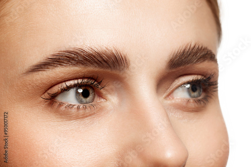 Close-up of beautiful clear female face with attractive gray eyes, perfect eyebrows and natural lashes. Eyebrow and lash lamination. Concept of makeup, cosmetics, natural beauty, skin care products photo