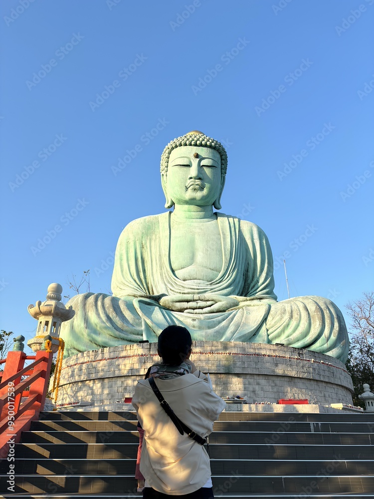 Fototapeta premium A teenage girl is standing and praying in front of the mock-up Daibutsu Buddha statue at Wat Phra That Doi Phra Chan temple, located on the serene hilltop in Mae Tha district, Lampang province of Thai