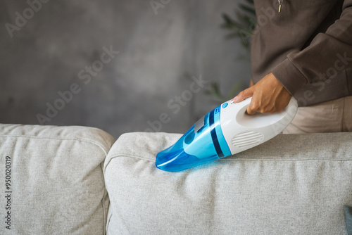 Unknown woman stand and vacuuming sofa with hand vacuum cleaner