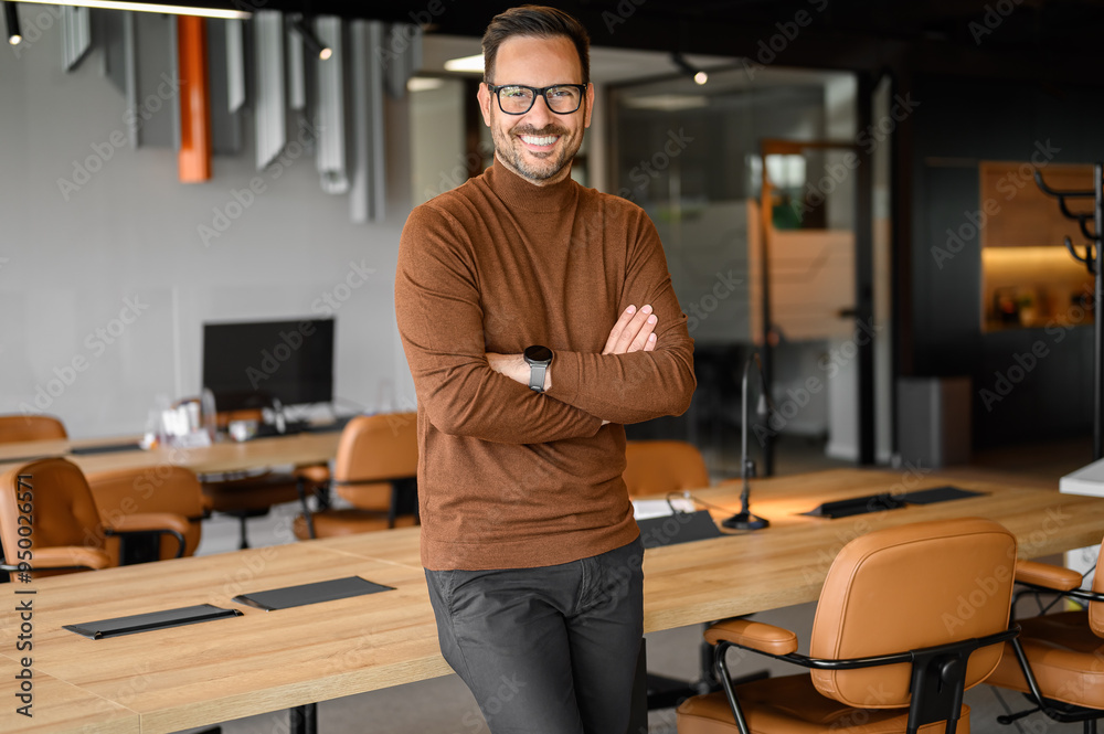 Portrait of handsome manager in eyeglasses and with arms crossed standing by conference table in office Portrait of handsome manager in eyeglasses and with arms crossed standing by conference table in office