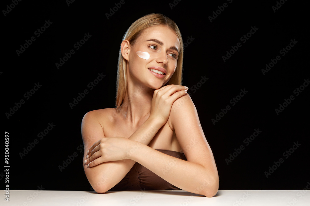 Fototapeta premium Radiant young woman with clear skin applying face cream, demonstrating role of effective skincare products in achieving smooth, glowing complexion. Concept of beauty, skincare, cosmetics