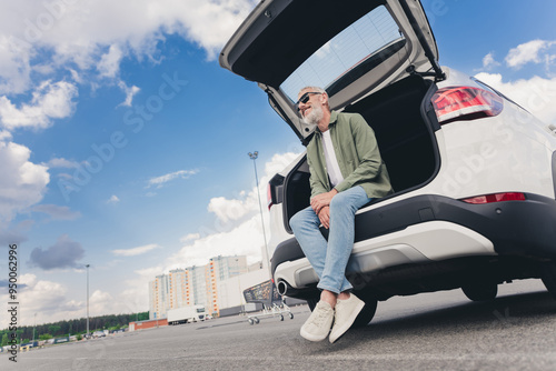 Photo of handsome good mood seniour guy wear green shirt sitting car trunk enjoy sunny weather outdoors urban city street photo