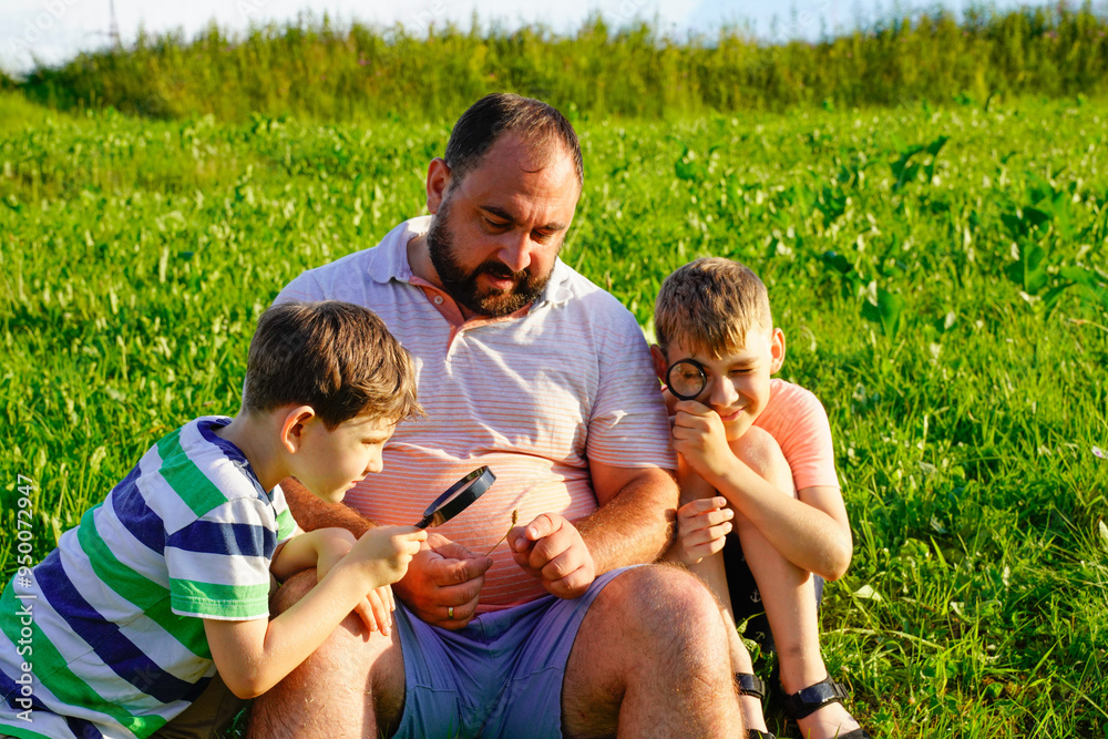 Father and sons exploring nature, looking at plants insects though magnifying glass Father and sons exploring nature, looking at plants insects though magnifying glass