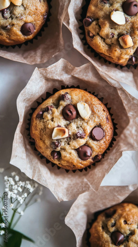 A beautifully presented batch of hazelnut and chocolate chip muffins, each wrapped in a delicate brown paper liner. The muffins are displayed against a white decor background, enhancing their 