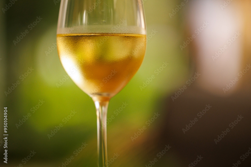 Obraz premium A sparkling glass of golden wine reflects the warmth of a lovely outdoor moment, inviting relaxation and joy.