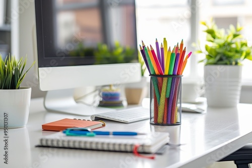 A desk setup with a computer, a notebook, and a cup of colorful pens