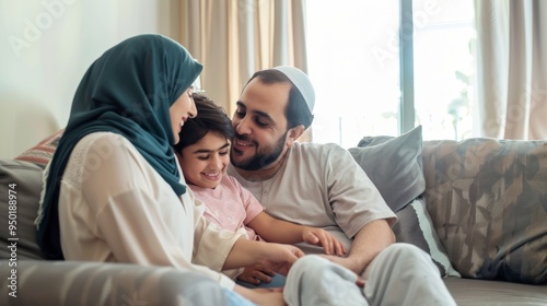 A family of three, a man, a woman and a child, are sitting on a couch. The man is wearing a white shirt and the woman is wearing a blue scarf. The child is smiling and the family appears to be happy