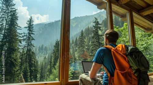 Man with a backpack working on a laptop in a mountain cabin, large window showing a scenic forest view, digital nomad, nature retreat