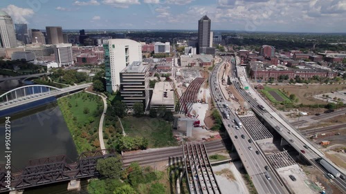 Drone aerial of new highway and multi land interstate construction coming soon and being built next to downtown and city center of Columbus, Ohio with turnpike car traffic and workers near buildings