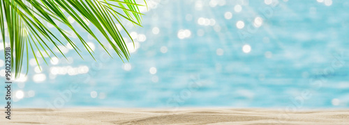 empty sand beach scene with glittering water background, defocused sunlights and green palm leaf border for product display backdrop, tropical summer day idyll