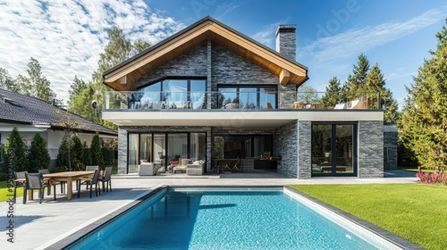 A beautifully designed country house with an open balcony door, garden furniture, a pool, and modern grey brick architecture