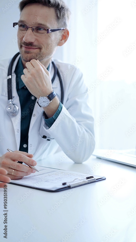 Obraz premium Doctor and a patient. The physician, wearing a white medical coat over a green shirt, gesturing with his hands during a consultation in the clinic. Medicine concept