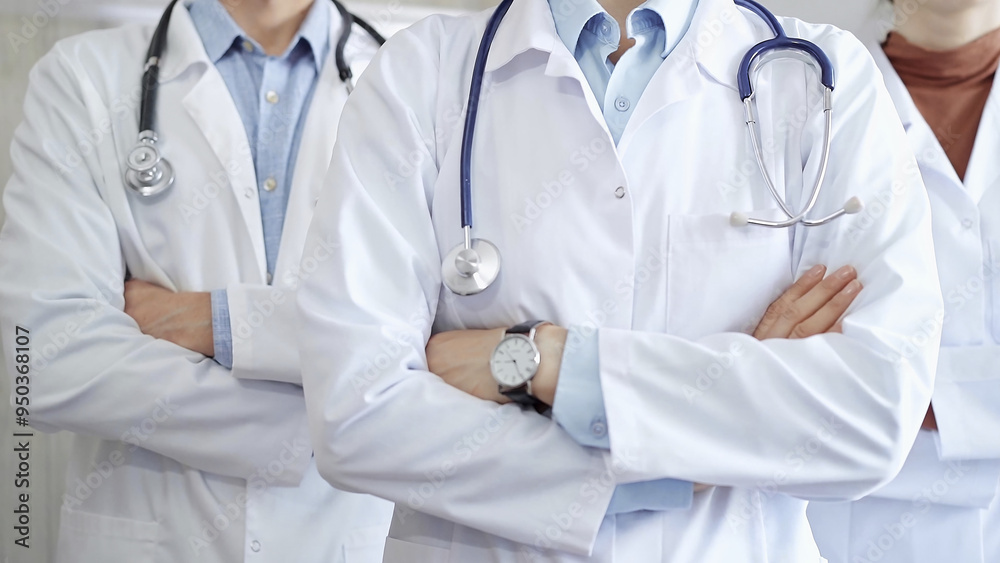 Group of doctors wearing white coats and stethoscopes standing with arms crossed. Medical team at work Group of doctors wearing white coats and stethoscopes standing with arms crossed. Medical team at work