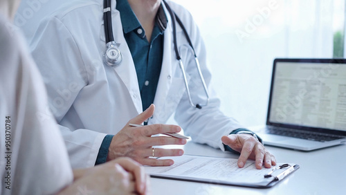 Doctor and a patient. The physician, wearing a white medical coat over a green shirt, is gesturing with his hands during a consultation in the clinic. Medicine