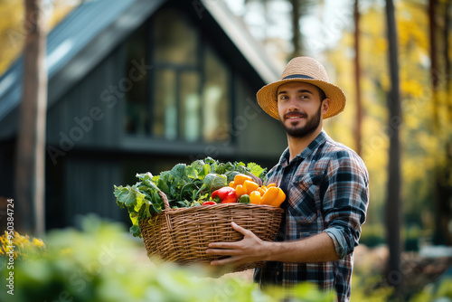 Middle-aged man holding a basket of harvest from his garden near his modern hous in the forest. Gardening peoples. Eco friendly nomad life style photo