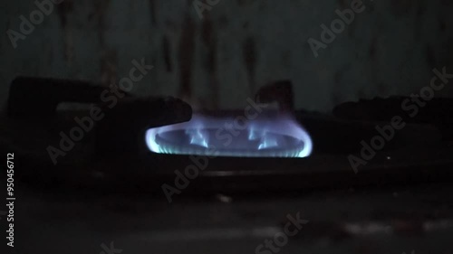 A single blue gas flame burns on a black stovetop in a dark kitchen.