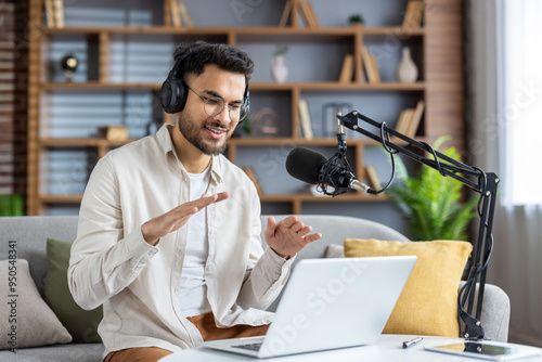 Confident young man recording podcast at home while using laptop and microphone, engaging with audience through live streaming and headphones photo