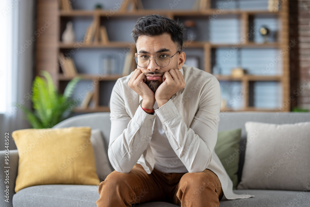 Thoughtful young man sitting on a sofa, reflecting on life decisions, wearing glasses and casual attire, conveying a sense of contemplation and introspection in a comfortable home setting Thoughtful young man sitting on a sofa, reflecting on life decisions, wearing glasses and casual attire, conveying a sense of contemplation and introspection in a comfortable home setting