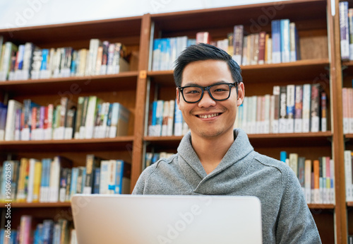 Laptop, portrait and Asian man in library for study with university, education and college scholarship. Books, online research and happy student on campus with learning, knowledge and growth in Japan