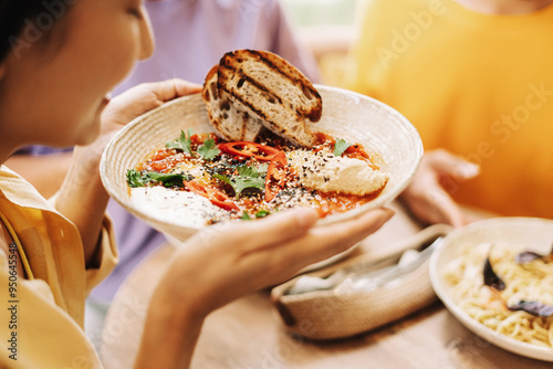 Fotografie Woman holding bowl of shakshuka with friends at restaurant