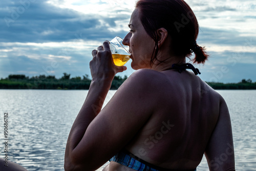 A woman enjoys a glass of spirits at a sunset by the water.