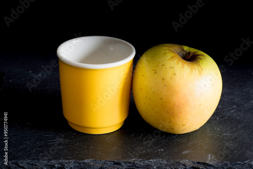 Yellow cup and tasty apple on a black stone surface against black background 
