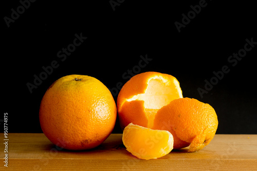 Oranges and orange wedge on a wooden table on a black background