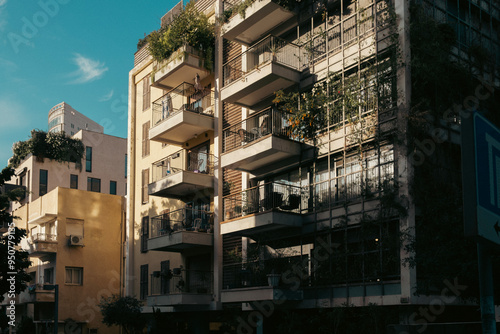 Sunlit urban scene showcasing modern and traditional architecture in Tel Aviv, Israel, with balconied apartments adorned with greenery under a clear blue sky. photo