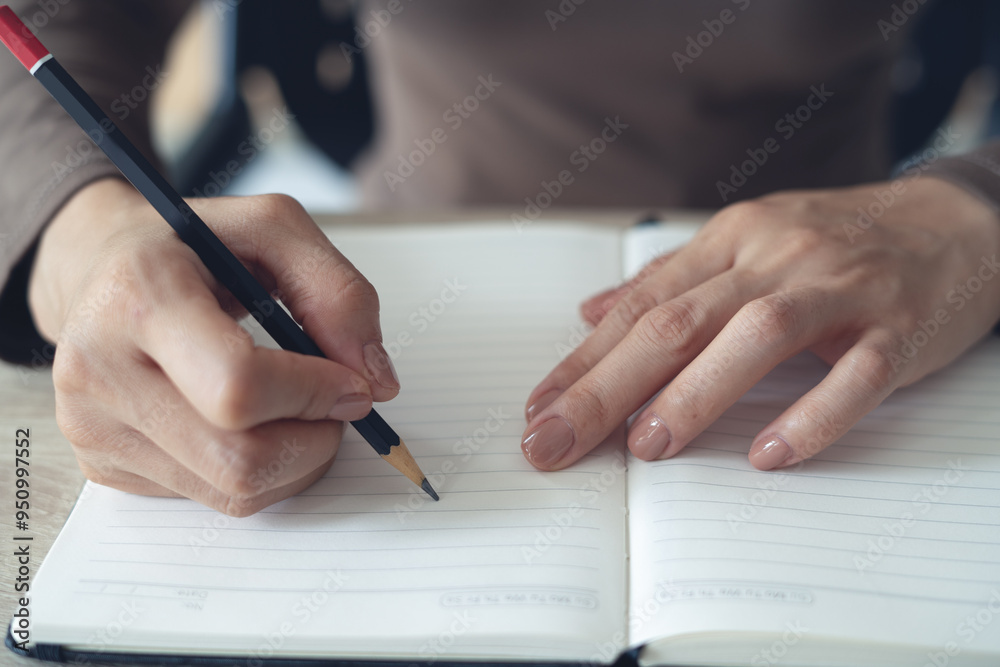 Close up, woman hand with a pencil writing on paper notebook on office table. Business woman note an idea on reminder notepad, business and event planing, front view Close up, woman hand with a pencil writing on paper notebook on office table. Business woman note an idea on reminder notepad, business and event planing, front view