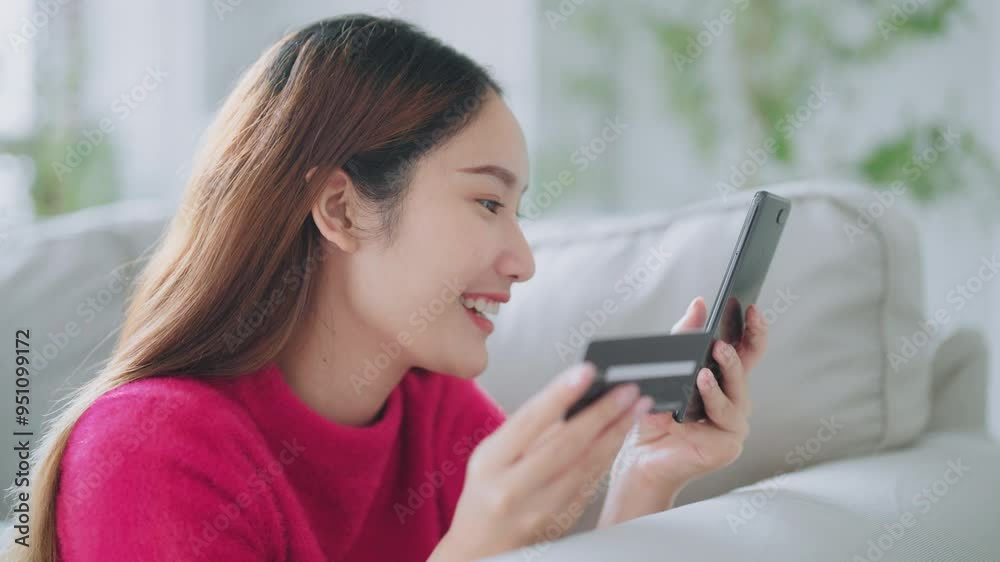 Young asian woman lying on sofa in living room, makes online banking payments through the internet from bank card on cell phone. Shopping online on mobile with credit card Young asian woman lying on sofa in living room, makes online banking payments through the internet from bank card on cell phone. Shopping online on mobile with credit card