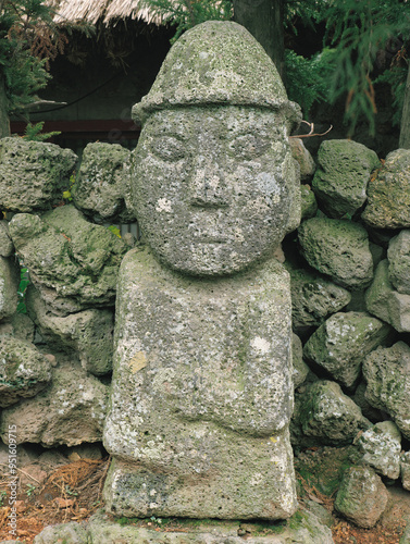 Seogwipo-si, Jeju-do, South Korea - August 1, 2006: Close-up of a Dolhareubang with volcanic rocks near the wall of house at Seongeup Folk Village photo