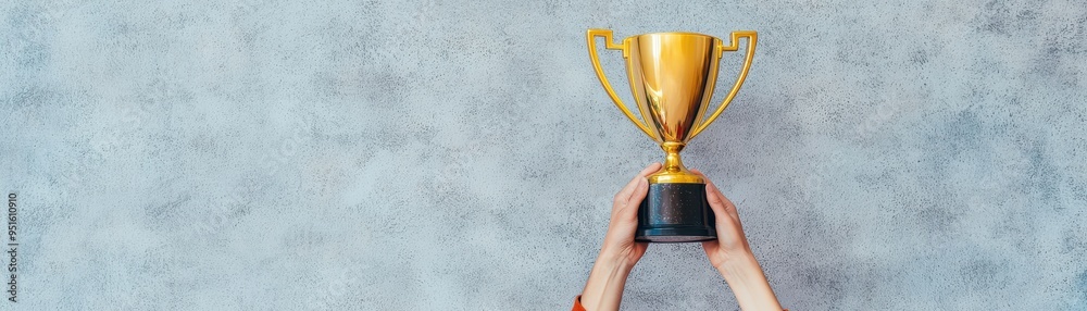 Φωτογραφία A person holding a shiny golden trophy against a gray background, symbolizing victory and achievement in competitions