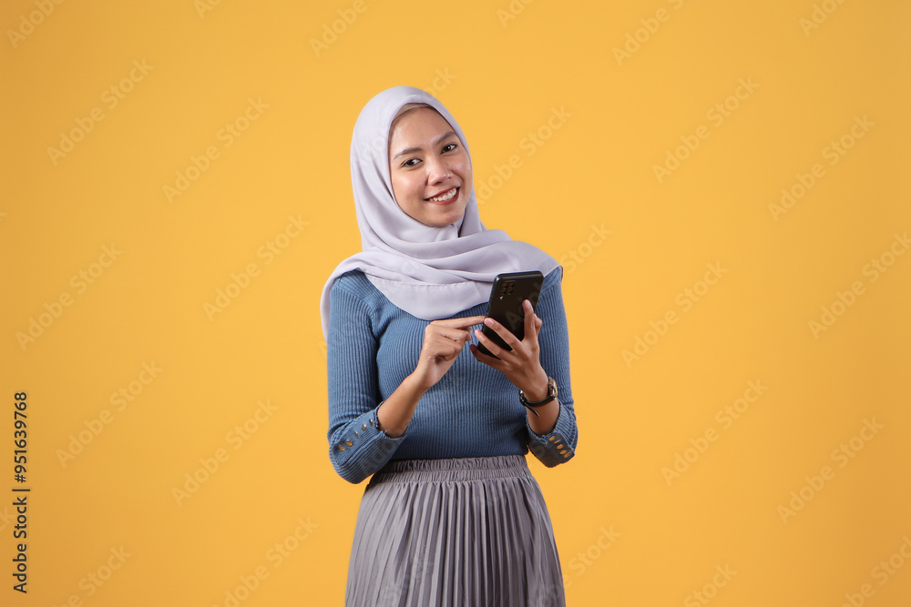 happy asian indonesian muslim woman holding smart phone on isolated yellow background happy asian indonesian muslim woman holding smart phone on isolated yellow background