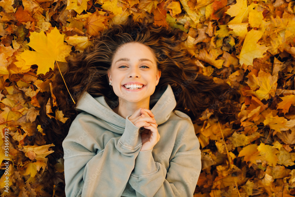 Smiling young woman lies on the autumn foliage in the forest with the yellow leaves