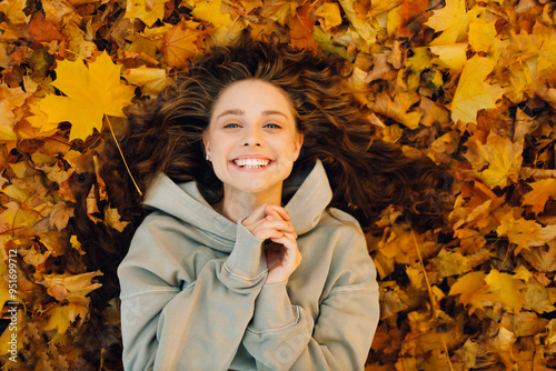 Obraz na płótnie Smiling young woman lies on the autumn foliage in the forest with the yellow leaves w salonie