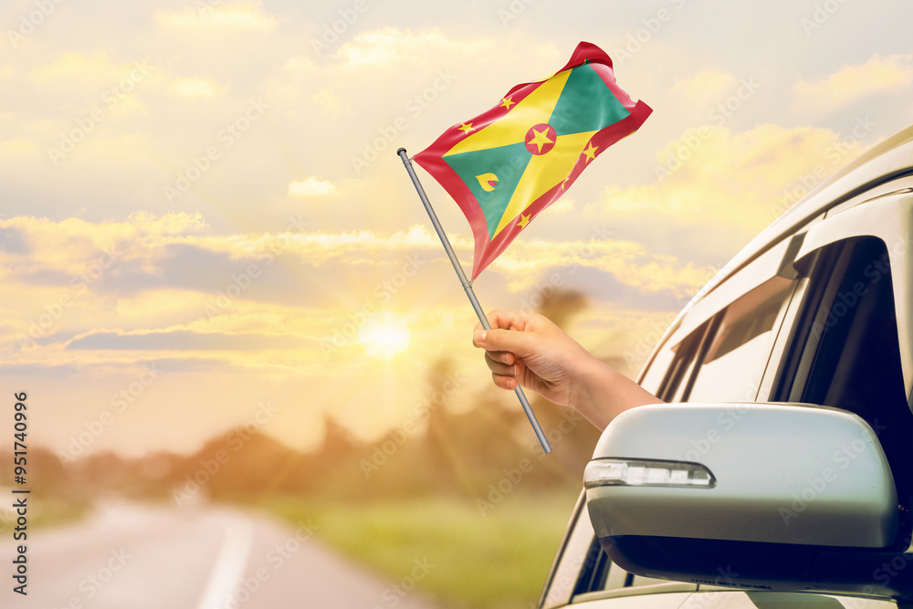Waving the Grenada flag against the sunrise or sunset from a car driving along a country road. Holding the Grenada flag, traveling by car, on a weekend trip. Waving the Grenada flag against the sunrise or sunset from a car driving along a country road. Holding the Grenada flag, traveling by car, on a weekend trip.