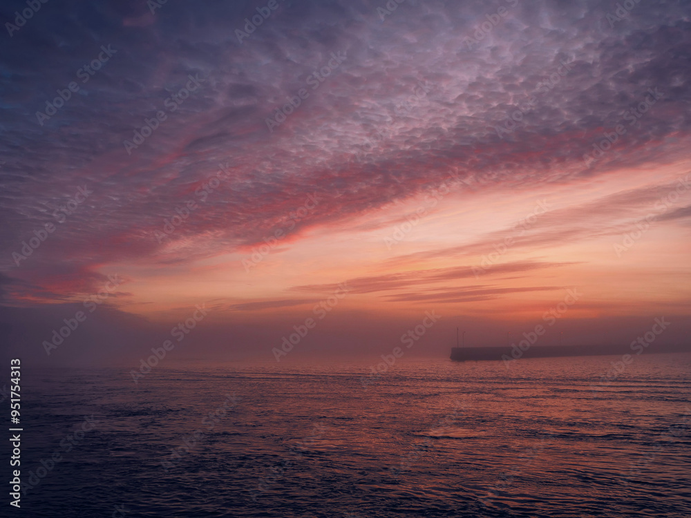 Fototapeta premium A yellow buoy sits in the ocean, surrounded by water. The sky is a beautiful mix of pink and purple hues, creating a serene and peaceful sunset atmosphere and mood. Nobody. Galway, Ireland.