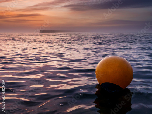 A yellow buoy sits in the ocean, surrounded by water. The sky is a beautiful mix of pink and purple hues, creating a serene and peaceful sunset atmosphere and mood. Nobody. Galway, Ireland. photo