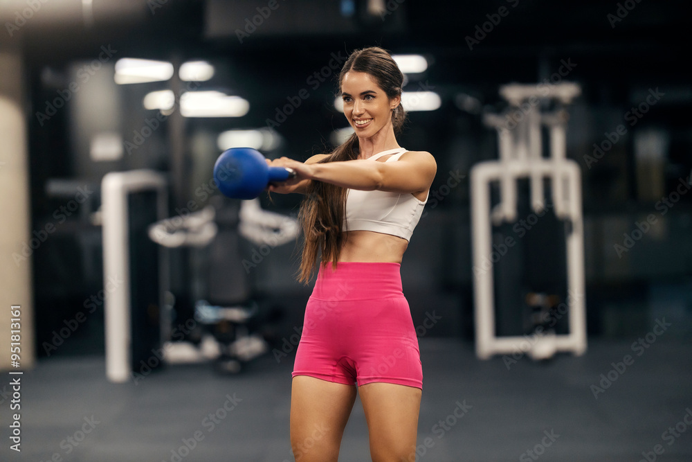 Smiling sportswoman in shape swinging with kettlebell at gym. Smiling sportswoman in shape swinging with kettlebell at gym.