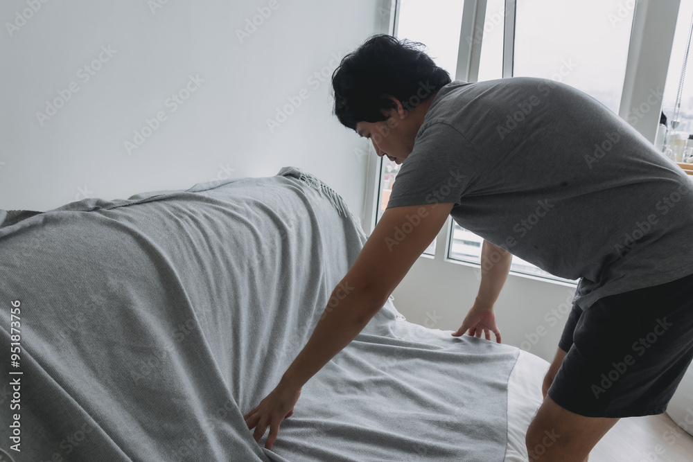 Asian man is doing his house work, covering the sofa with grey sheet. Asian man is doing his house work, covering the sofa with grey sheet.