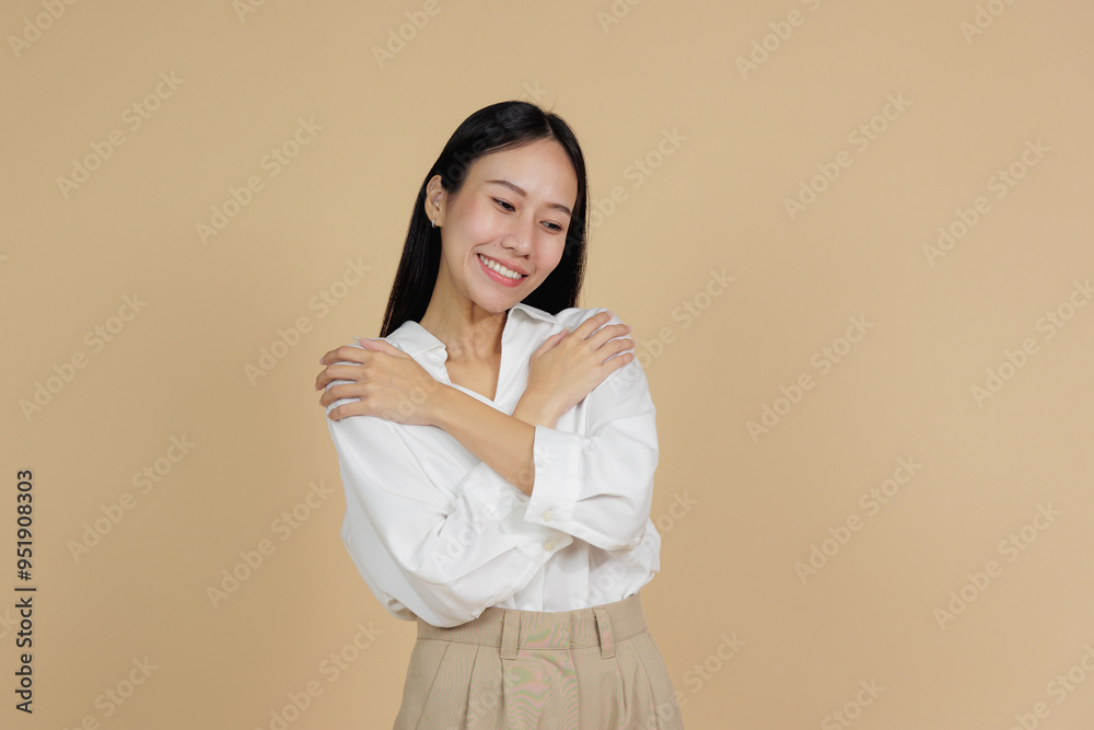 Smiling Woman Hugging Herself in a Warm Gesture, Beige Background Smiling Woman Hugging Herself in a Warm Gesture, Beige Background