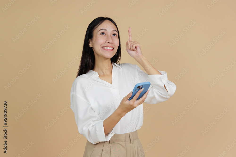 Cheerful Asian Woman Pointing Upwards While Using Smartphone Cheerful Asian Woman Pointing Upwards While Using Smartphone